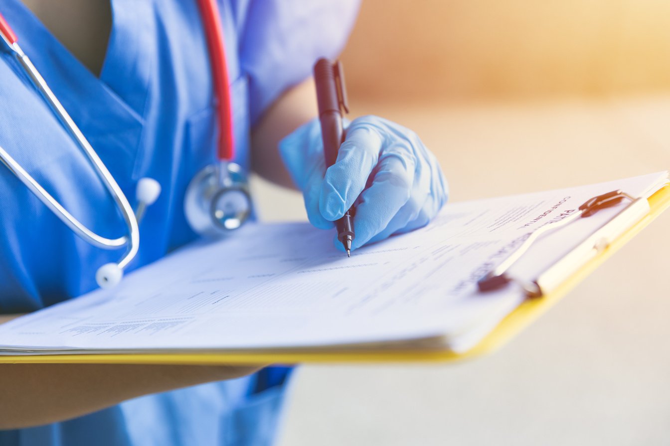 a doctor in blue scrubs writing on a clipboard